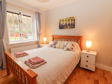 A bedroom with a wooden bed frame two bedside tables with lamps and a window with curtains at Hazelwood in Leap County Cork