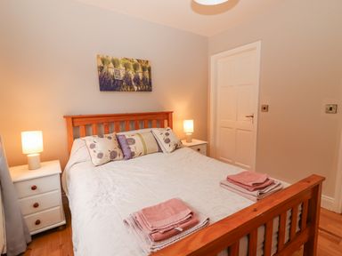 A bedroom with a wooden bed frame white bedding floral pillows two bedside tables with lamps and folded towels on the bed at Hazelwood in Leap County Cork