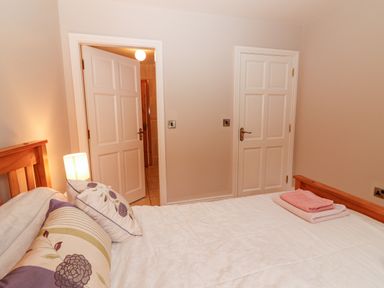 A bedroom with a wooden bed a lamp on a bedside table pillows and towels on the bed two white doors on the wall Hazelwood Leap County Cork