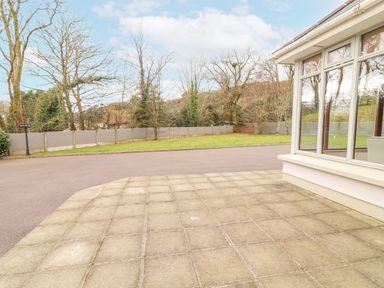 A tiled patio area adjacent to a paved driveway with a lawn and trees enclosed by a fence at Hazelwood in Leap County Cork