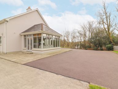 A driveway and patio outside a house with a glass enclosed porch and leafless trees in the background at Hazelwood in Leap County Cork