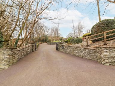 A paved driveway with low stone walls and gate leading to a house with trees and bushes at Hazelwood in Leap County Cork
