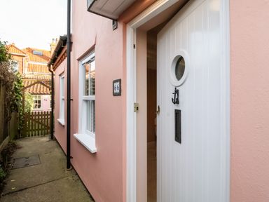 A narrow walkway between two pink houses leading to a wooden gate with house number 64 visible