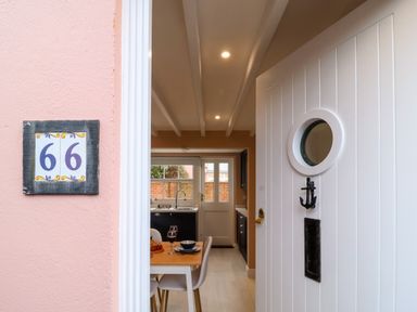 An open white front door with a small round window looking into a kitchen and dining area with a table set for two at Poppy Cottage in Southwold