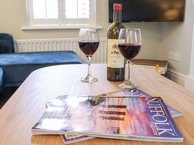 A table with two glasses of red wine a bottle and magazines in a living room at Poppy Cottage in Southwold