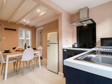 A kitchen and dining area with a table set for two white chairs a retro refrigerator a stovetop with pots and a sink at Poppy Cottage in Southwold