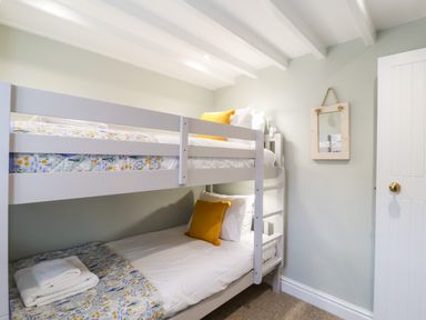 A small bedroom with white bunk beds yellow pillows and folded towels on the lower bed at Poppy Cottage in Southwold