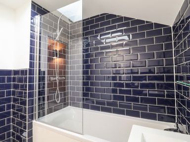 A bathroom with a bathtub and showerhead with black and dark blue tiled walls at Poppy Cottage in Southwold
