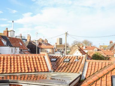 A view of red tiled rooftops and chimneys in a residential area under a blue sky at Poppy Cottage in Southwold