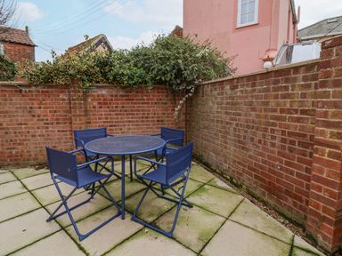 An outdoor patio area with a round table and four blue chairs surrounded by brick walls at Poppy Cottage in Southwold