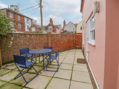 A small outdoor patio with four blue chairs and a round table surrounded by brick walls and a pink building at Poppy Cottage in Southwold