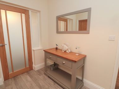 A hallway with a wooden door mirror above a wooden console table with decorative fish and bird figures at Bamburgh Dunes Bamburgh near Seahouses