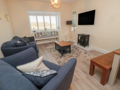 A living room with blue sofas a wooden coffee table a rug and a wall-mounted television at Bamburgh Dunes Bamburgh near Seahouses