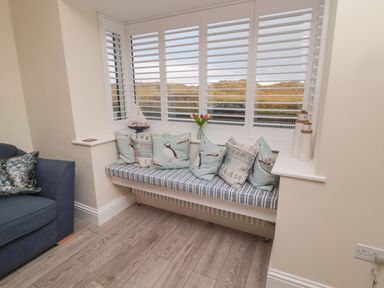 A corner window seat with cushions next to a blue armchair in a room at Bamburgh Dunes Bamburgh near Seahouses