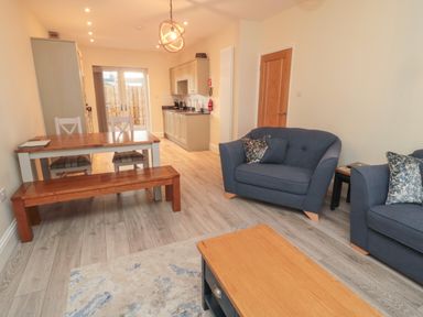 A dining table with chairs and bench and a blue sofa set in a room with kitchen cabinets at Bamburgh Dunes Bamburgh near Seahouses