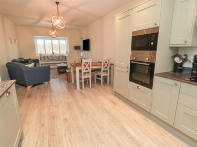 A kitchen and dining area with built in oven and microwave a wooden dining table with chairs and a sitting area with sofas a window with a bench at Bamburgh Dunes Bamburgh near Seahouses