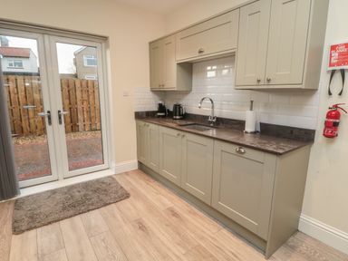 A kitchen with cabinets a countertop a sink a kettle a coffee machine a fire extinguisher and glass doors opening to a fenced yard at Bamburgh Dunes Bamburgh near Seahouses
