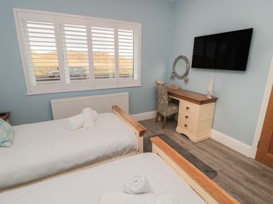 A bedroom with two single beds with white linens a desk with a chair a wall-mounted TV and a window with shutters at Bamburgh Dunes Bamburgh near Seahouses