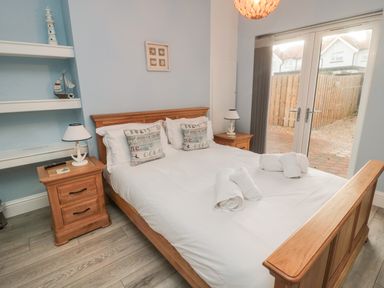 A bedroom with a wooden double bed with white bedding and rolled towels two bedside tables with lamps and a glass door leading outside at Bamburgh Dunes Bamburgh near Seahouses