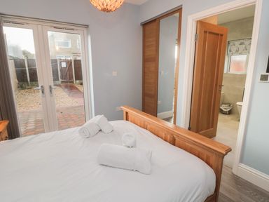 A bedroom with a wooden bed frame white bed linens and rolled towels on the bed glass doors leading outside a wooden door open to a bathroom and a wooden wardrobe with mirrored sliding doors at Bamburgh Dunes Bamburgh near Seahouses