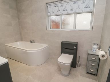 A bathroom with a bathtub toilet small cabinet and window with patterned blind at Bamburgh Dunes Bamburgh near Seahouses