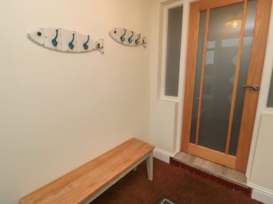 An entryway with a wooden bench below fish-shaped wall hooks and a wooden door with frosted glass panels at Bamburgh Dunes Bamburgh near Seahouses