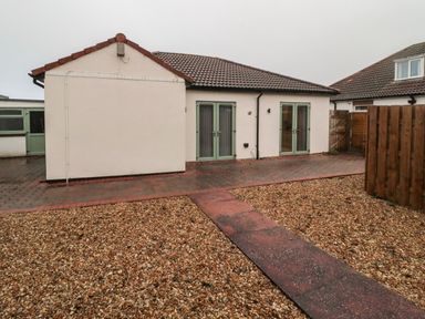 A backyard with gravel and a paved walkway leading to a single story house with two sets of double doors at Bamburgh Dunes Bamburgh near Seahouses