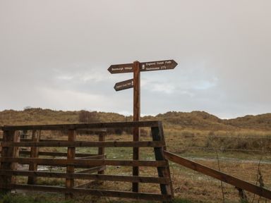 A wooden signpost with directional signs and a wooden fence in a grassy area at Bamburgh Dunes Bamburgh near Seahouses