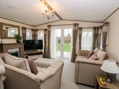 A living room with two beige sofas a television on a stand a fireplace a mirror and glass doors at Hudson's Hideaway in South Lakeland Leisure Village