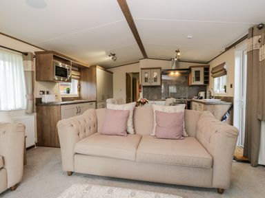 A living room with a beige sofa and pillows facing an open kitchen with cabinets and appliances at Hudsons Hideaway in South Lakeland Leisure Village