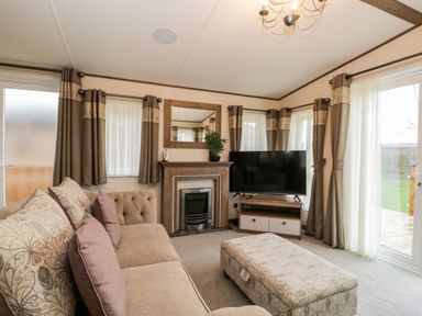A living room with a sofa ottoman fireplace television and curtains at Hudson's Hideaway in South Lakeland Leisure Village