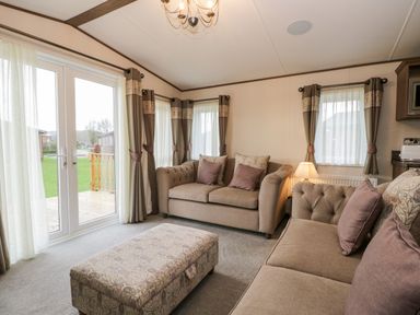 A living room with two sofas an ottoman a lamp and windows with curtains at Hudson's Hideaway in South Lakeland Leisure Village