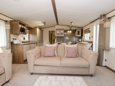 A living room with a beige sofa and kitchen in the background at Hudson's Hideaway in South Lakeland Leisure Village
