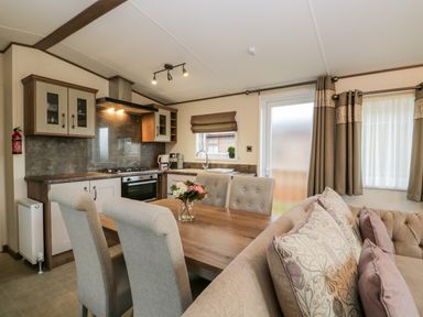 A kitchen and dining area with a wooden table and upholstered chairs and a sofa with patterned cushions at Hudson's Hideaway in South Lakeland Leisure Village