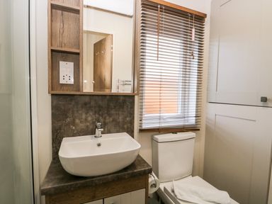 A bathroom with a sink and faucet a toilet with a towel on top a window with blinds and a cabinet at Hudson's Hideaway in South Lakeland Leisure Village
