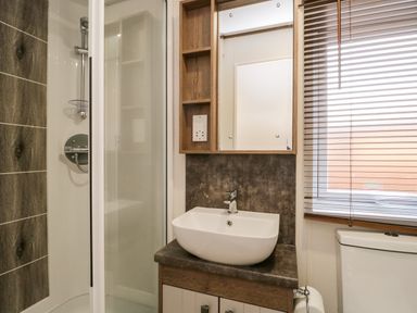 A bathroom with a shower, sink, mirror, window with blinds, and toilet at Hudson's Hideaway in South Lakeland Leisure Village