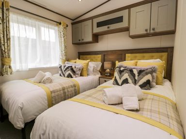 A bedroom with two single beds and a window with floral curtains at Hudson's Hideaway in South Lakeland Leisure Village