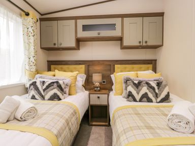 A bedroom with two single beds a bedside table and overhead cabinets at Hudson's Hideaway in South Lakeland Leisure Village