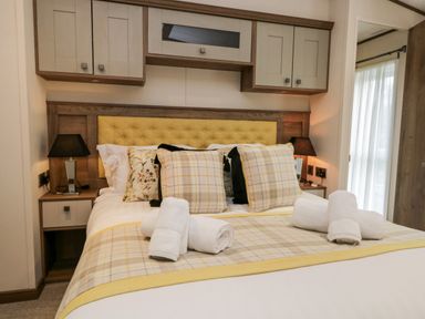 A bedroom with a bed with yellow and plaid pillows and rolled white towels at Hudson's Hideaway in South Lakeland Leisure Village