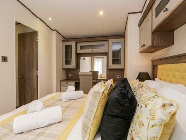 A bedroom with a bed, multiple cushions, rolled towels on the bed, a dressing table with cabinets and a chair at Hudson's Hideaway in South Lakeland Leisure Village