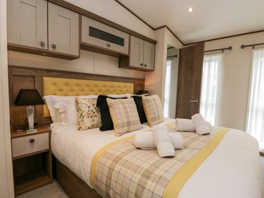 A bedroom with a bed with pillows and rolled towels a bedside table with a lamp and cabinets above the headboard at Hudsons Hideaway in South Lakeland Leisure Village