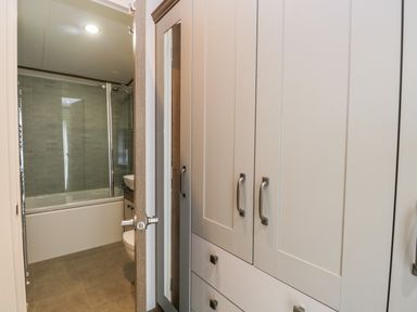 A bathroom with a bathtub shower combination and a closet with cupboards and drawers at Hudson's Hideaway in South Lakeland Leisure Village