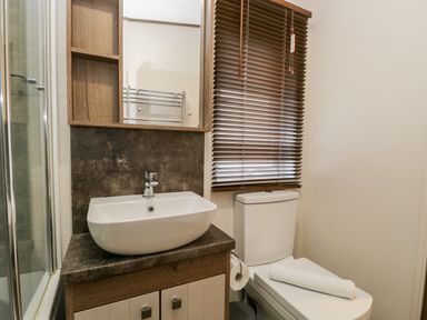 A bathroom with a sink on a cabinet next to a toilet with a towel a window with blinds and a shower with a glass door at Hudson's Hideaway in South Lakeland Leisure Village