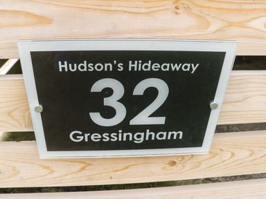 A sign with the text Hudson's Hideaway 32 Gressingham on a wooden surface at Hudson's Hideaway in South Lakeland Leisure Village