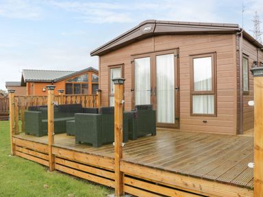 A wooden deck with outdoor wicker furniture outside a brown cabin at Hudson's Hideaway in South Lakeland Leisure Village