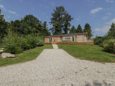 A wooden house with a gravel driveway and grass lawn surrounded by trees at 2 Faraway Fields in Dobwalls