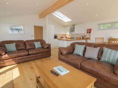 A living room with two brown leather sofas and a wooden coffee table next to a kitchen at 2 Faraway Fields in Dobwalls
