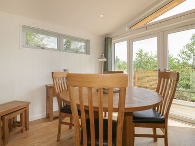 A dining area with a wooden round table and chairs near glass doors and a window at 2 Faraway Fields in Dobwalls