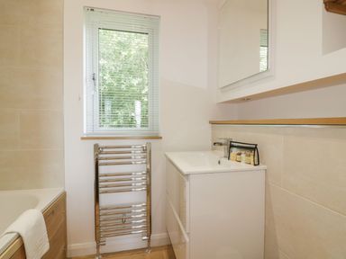 A bathroom with a bathtub a towel radiator window and a sink with toiletries at 2 Faraway Fields in Dobwalls