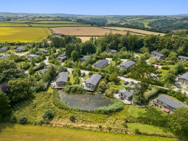 A rural holiday park with small houses arranged around a pond and surrounded by fields at 2 Faraway Fields in Dobwalls